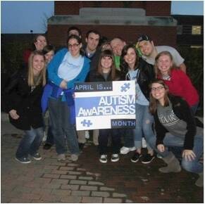 Student Accessibility Resources staff posing with an Autism Awareness Month poster in front of the Carillon Clocktower